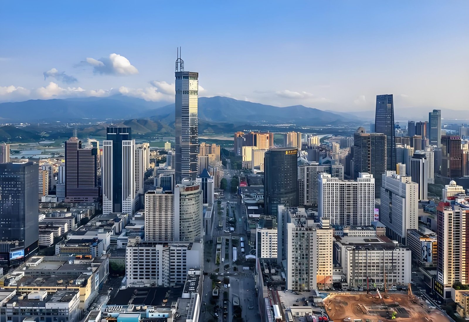 Daytime skyline of Shenzhen with office buildings and mountains in the background.