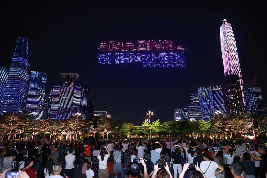 Shenzhen skyline at night with an illuminated Amazing Shenzhen display above the crowd.